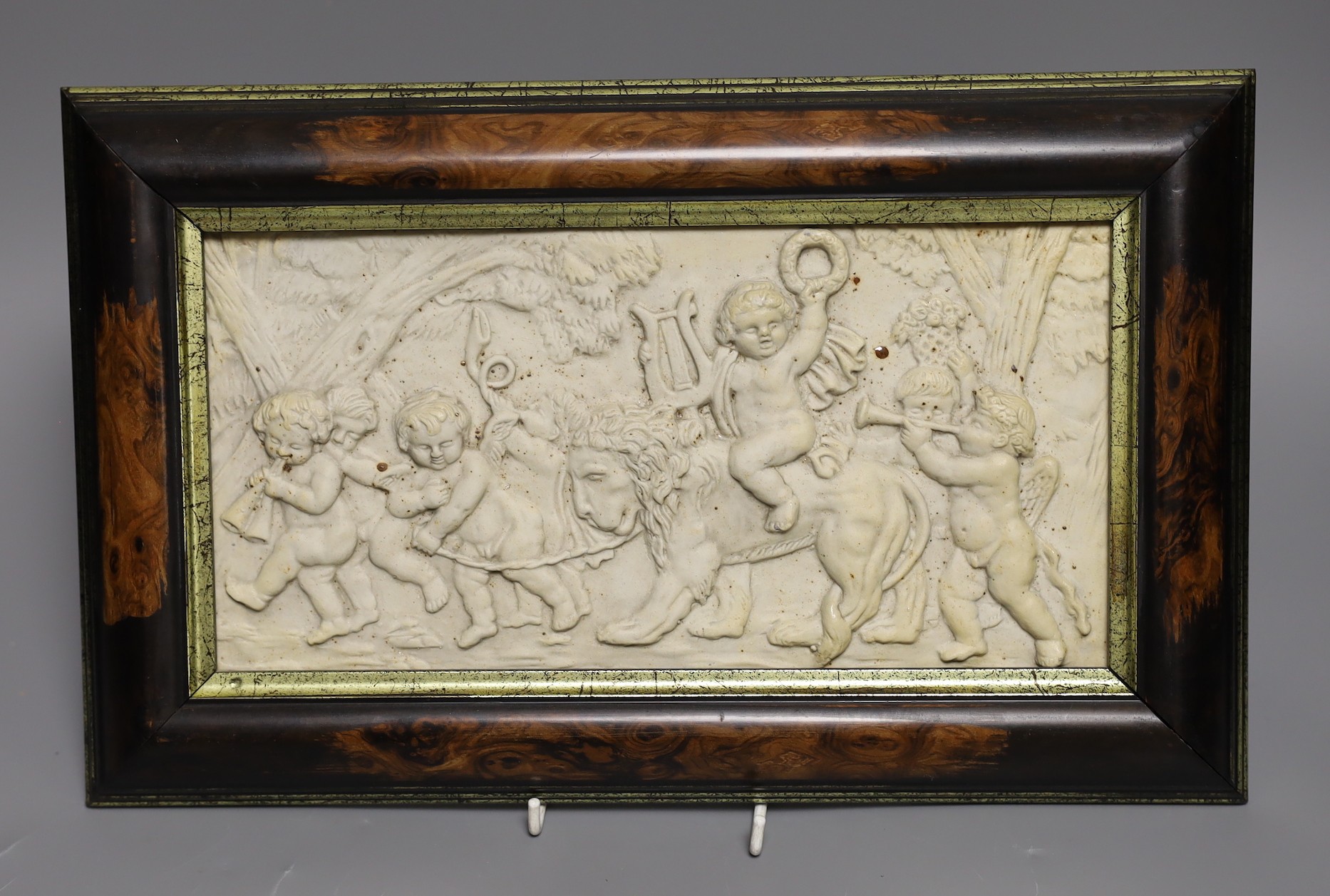 A framed ceramic relief plaque of classical scene with putti 16x31cm excl frame